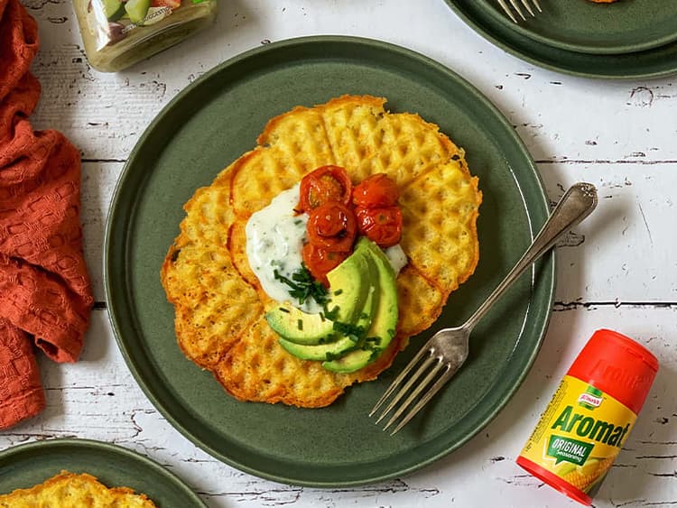 A waffle topped with avocado and tomatoes on a green plate