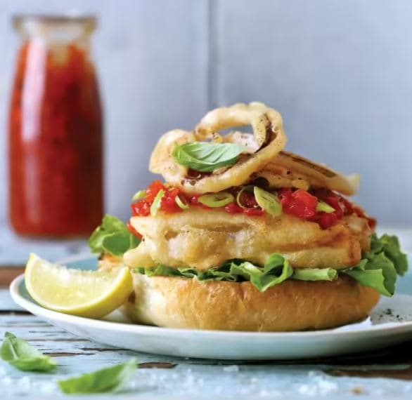 A sandwich on a plate with onion rings on top