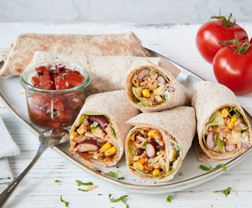 A white plate topped with a burrito next to a jar of salsa
